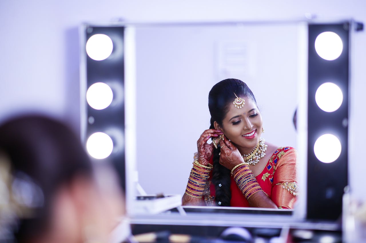 Captivating Indian bride adorned in traditional attire, smiling at her reflection while preparing for a wedding ceremony.
