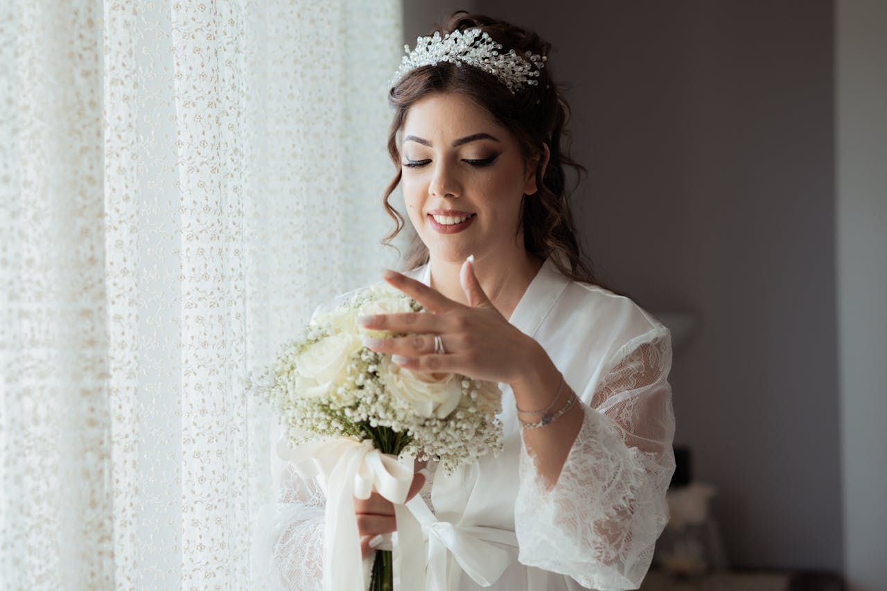 A smiling bride admires her floral bouquet indoors. Elegant and serene wedding moment.