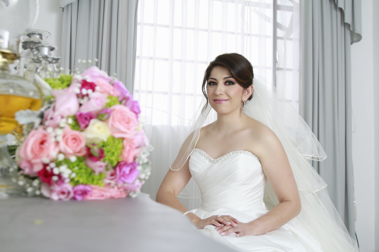 A beautiful bride in a white gown, posing indoors with a colorful bouquet.